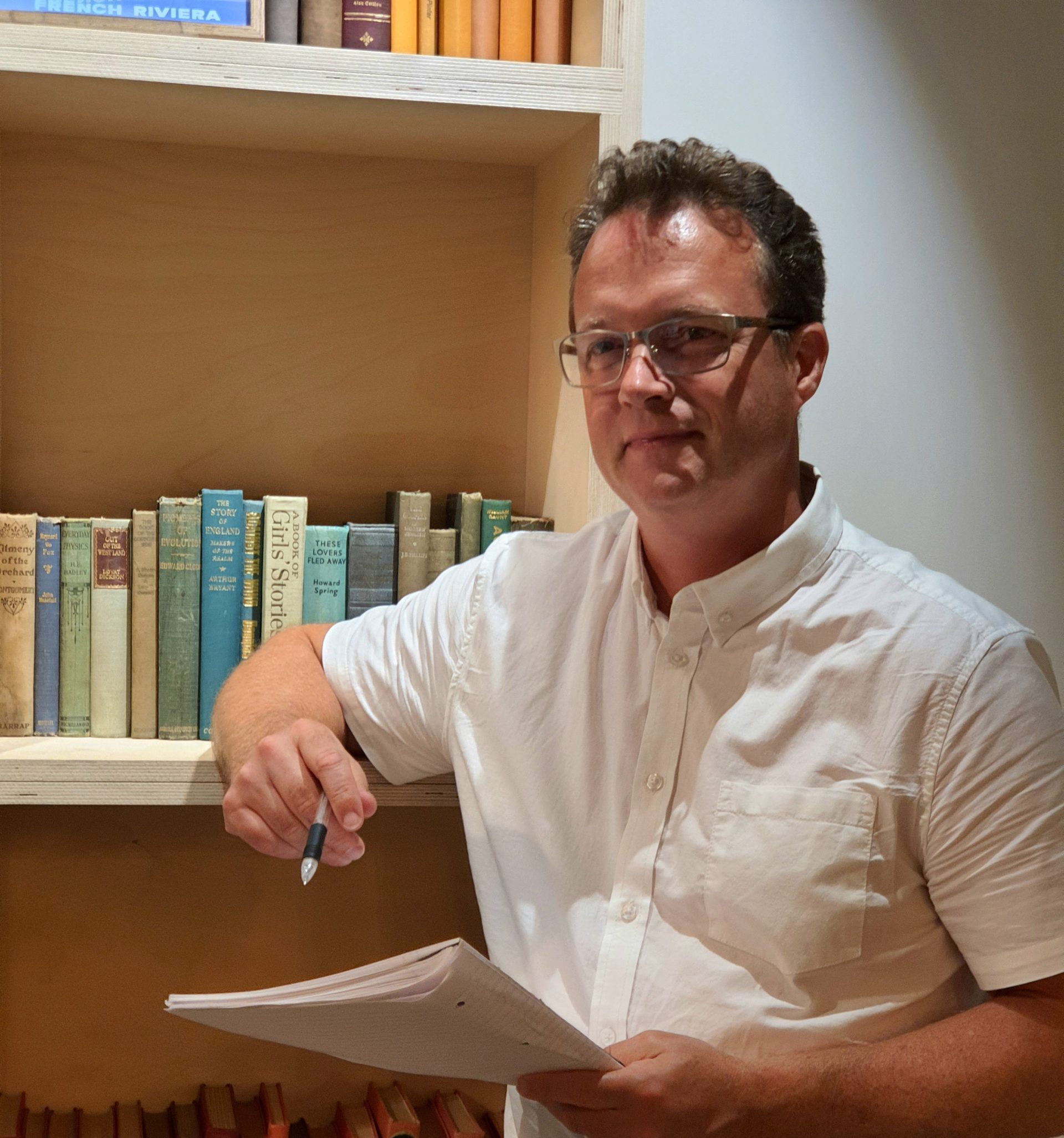 David leans on a bookshelf as he takes notes - Tech Recruitment Agency